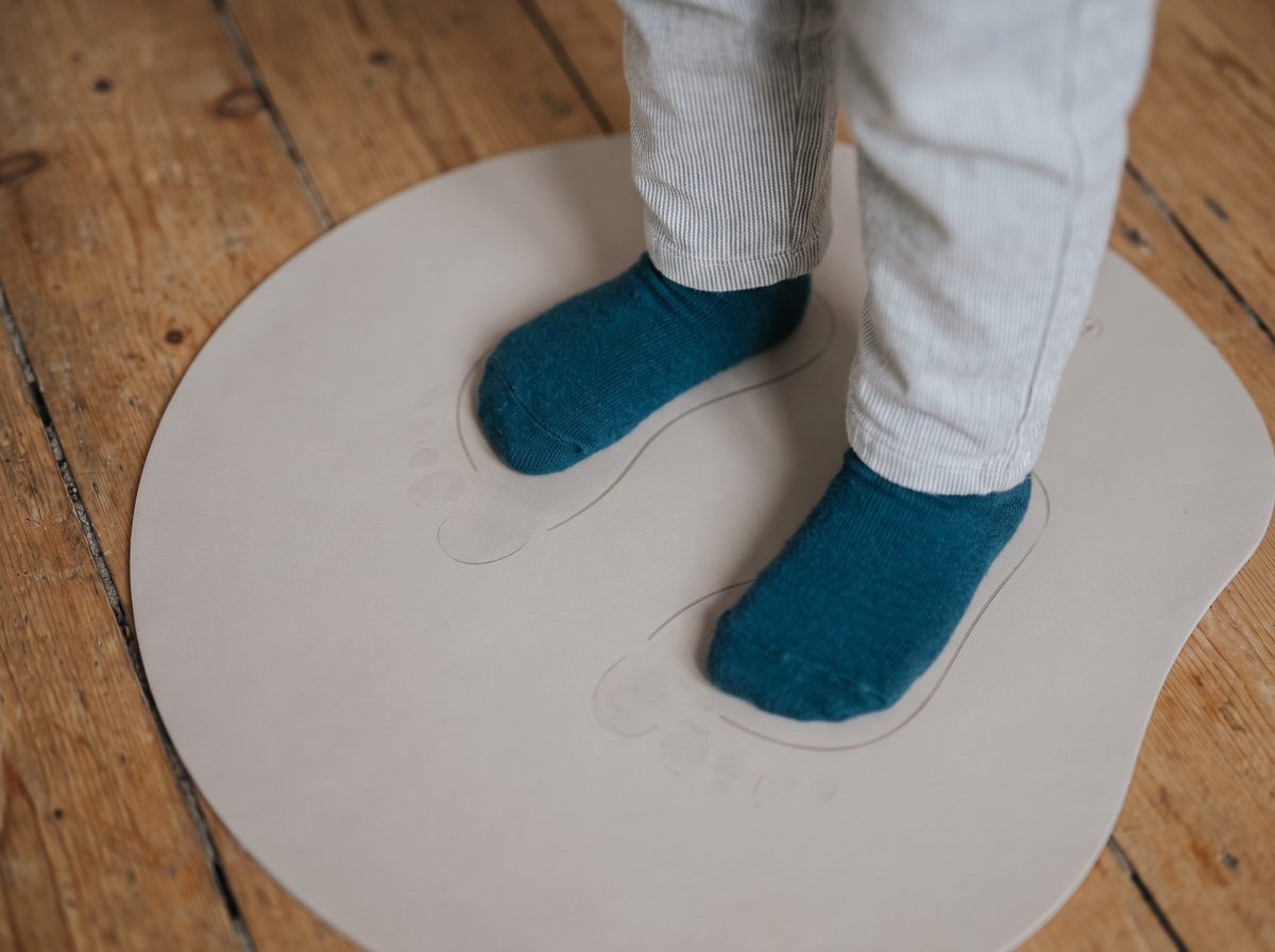 Pies de un niño, con medias, sobre una alfombra con huellas dibujadas